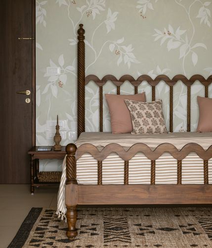 Carved wooden four-poster bed with scalloped rails against floral wallpaper, pink cushions, jute rug