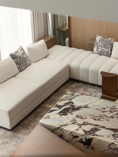 Cream sectional sofa with patterned pillows beside a veined marble coffee table and wood-panelled wall