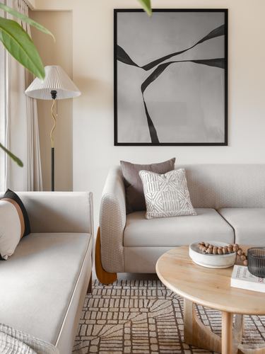 Neutral living room corner with two beige sofas, round wood table, and abstract framed art above