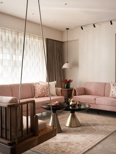Pink velvet sofas around brass pedestal tables with a wooden swing in foreground of a Pune living room