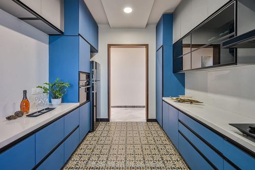 Galley kitchen with blue cabinetry, white countertops, and patterned tile floor leading to hallway