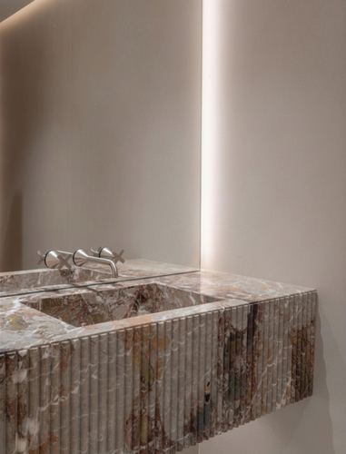Close-up of a fluted stone bathroom vanity with cross-handle faucet under a vertical wall light