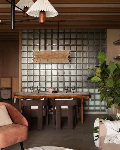 Dining nook with glass block wall, pleated pendant lights, wooden table and dark chairs