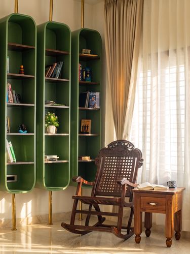 Wooden cane rocking chair beside a side table, in front of tall green capsule-shaped bookshelves