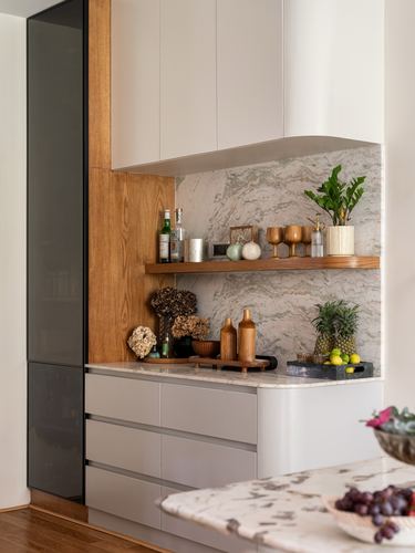Kitchen corner with marble backsplash, wood shelf styled with glassware and plants, grey cabinetry below