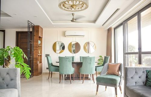 Open-plan living-dining room with sage green velvet chairs, round mirrors, gold chandelier and marble floor