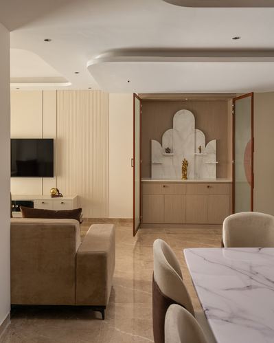Beige living room opening to an arched pooja niche with marble table in foreground