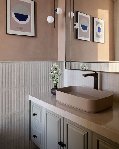 Pink bathroom vanity with oval basin, fluted tile wall, and framed geometric prints
