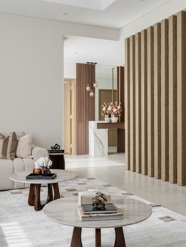 Living room with round marble coffee tables, beige sofa, and wood slat divider wall leading to foyer