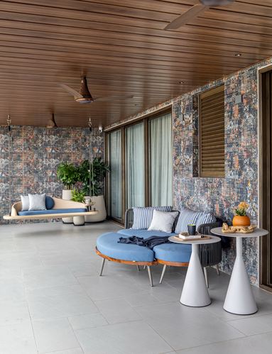 Covered balcony with blue curved sofa, hanging swing, patterned wall tile, and wood-slat ceiling.