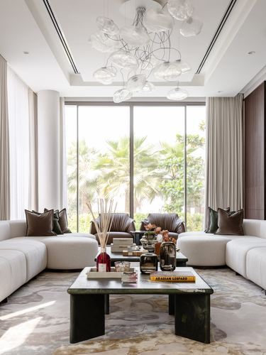 Neutral living room with two cream sofas, leather armchairs, and a green stone coffee table before floor-to-ceiling windows