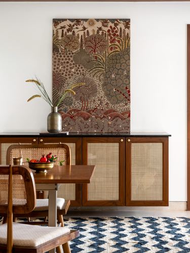 Dining nook with cane-front sideboard, framed textile art, brass vase and chevron rug