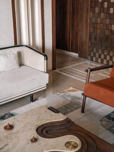 Curved cream sofa and orange armchair around a sculptural stone coffee table in Ahmedabad living room