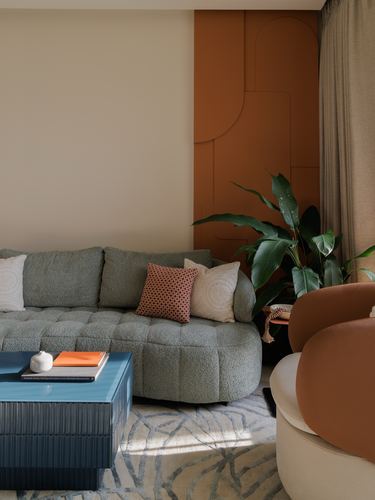 Sage boucle sectional sofa against a raised orange geometric panelled wall with a plant and blue lacquered coffee table