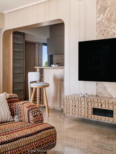 Living room with patterned sofa, wood archway to kitchen, and fluted stone TV wall