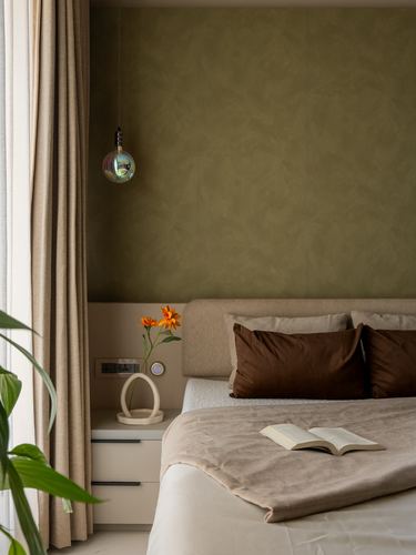 Bedroom corner with olive plaster wall, beige bed, brown pillows, and hanging pendant light