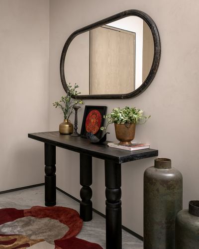Black console table below oval mirror with plants, brass vase, and framed art in foyer