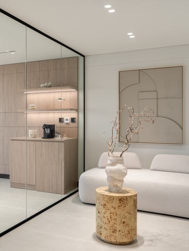 Beige sofa with sculptural vase on burl side table beside glass-partitioned wood cabinetry nook