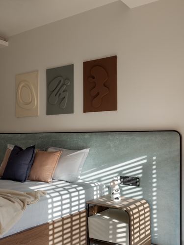 Bedroom corner with sage velvet headboard, textured wall art, and striped window light