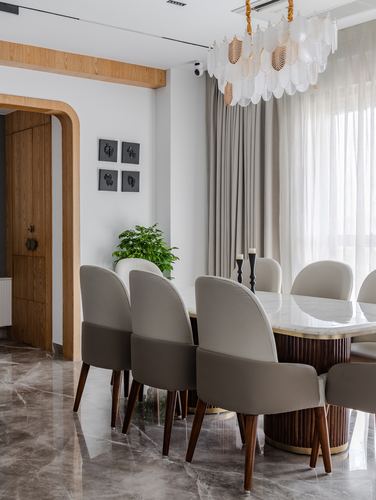 Dining room with marble table, fluted wood base, taupe chairs, sculptural leaf chandelier, arched wood door