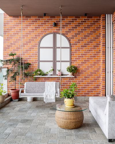 Balcony seating area with hanging swing, rattan coffee table, and brick wall with arched window detail.
