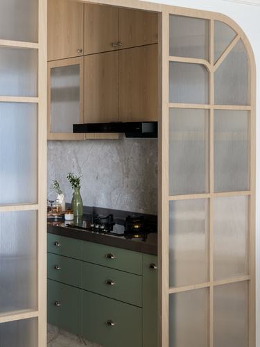 Kitchen niche framed by arched fluted glass doors, wood cabinets above, green drawers below