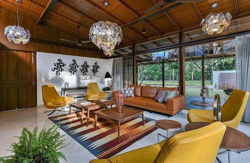 Living room with yellow leather chairs, tan sofa, kilim rug, wood ceiling, and crystal chandeliers opening to garden