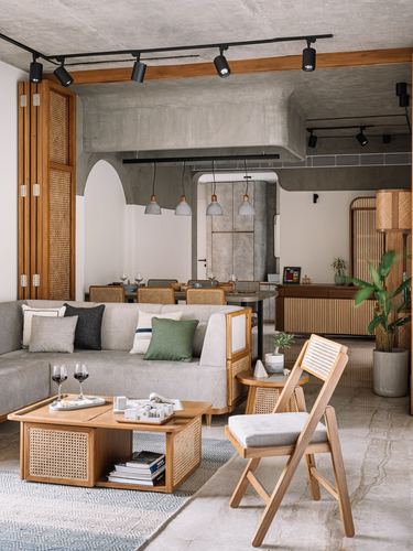 Living room with cane sofa, wooden folding chair and concrete ceiling, dining area visible beyond arch