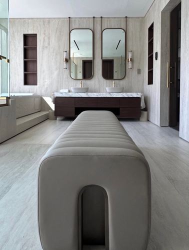Symmetrical marble bathroom with double vessel sinks, hanging mirrors, and a large ribbed bench