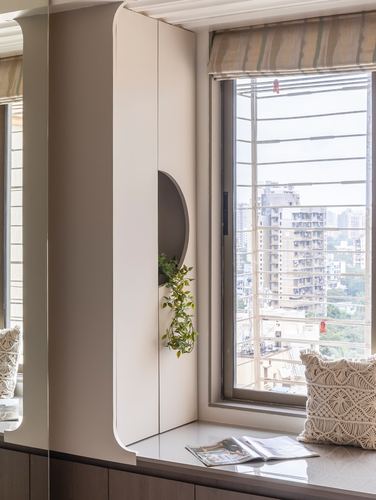 Curved white cabinetry with circular plant niche beside a window seat overlooking a city view