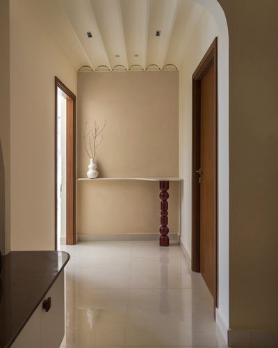 Curved beige corridor with fluted ceiling, wooden doors, and a console table on a maroon sculptural leg