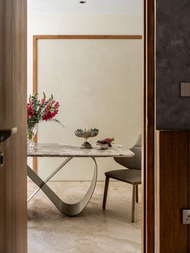 View through doorway into dining area with marble table, sculptural base, and flowers