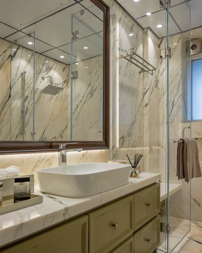 Marble bathroom with olive vanity, white vessel sink, backlit stone wall and glass shower