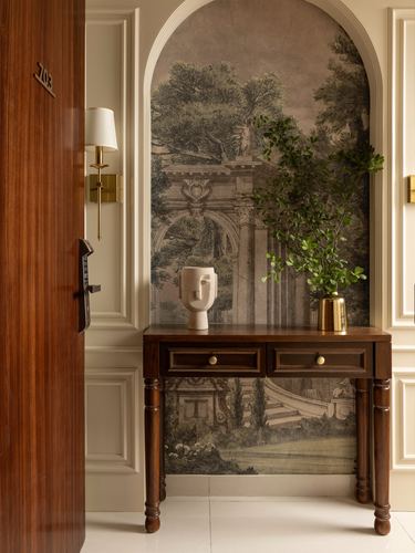 Arched niche with classical mural wallpaper above wooden console table in entry foyer