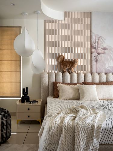 Bedroom with scalloped beige headboard, fluted panel wall, pendant lights, and a cat perched above the bed