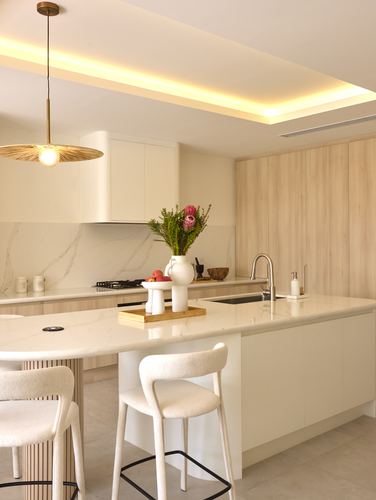 Light-filled kitchen with wood cabinetry, marble-look island, cove ceiling lighting, and boucle bar stools