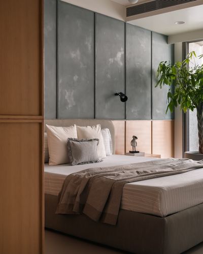 Bedroom with grey textured paneled headboard wall, wooden door frame, and layered neutral bedding