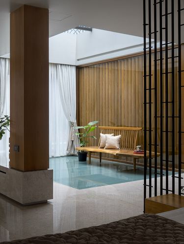Foyer with wooden bench, sheer curtains, wood-louvered wall and skylight above, marble floor with glass strip