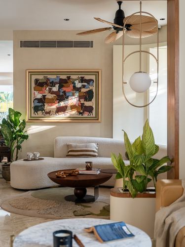 Curved cream boucle sofa with round wood coffee table beneath a folk art painting and sculptural pendant light