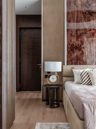Bedroom corner with leather headboard, round side table, brass lamp, and burl wood panel
