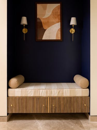 Daybed with bolsters in a navy niche below abstract art and brass sconces