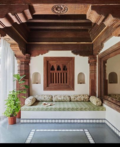 Carved wooden ceiling and columns frame a built-in bench seat with block-print cushions in a Mumbai home
