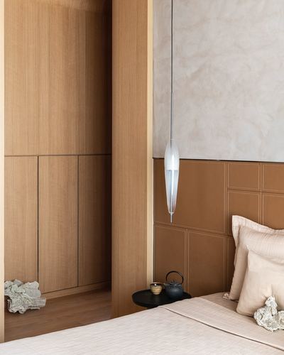 Bedroom corner with wood wardrobe, quilted leather headboard, and hanging glass pendant light