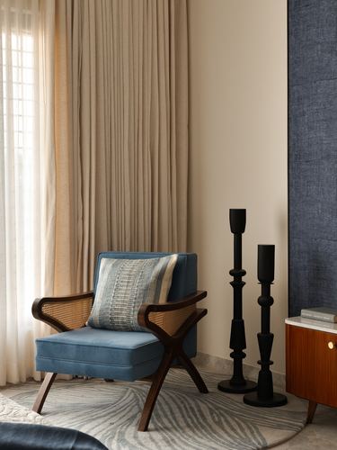 Blue cane armchair with cushion beside tall black candlesticks against navy wall panel