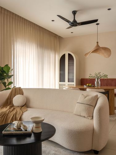 Curved cream boucle sofa in living room with arched cabinet, woven pendant, and dining area beyond
