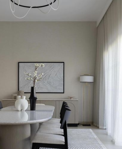 Beige-toned dining area with stone table, black chairs, floor lamp, and framed textured art