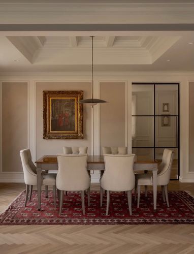 Formal dining room with upholstered chairs, gilt-framed painting, and red patterned rug on herringbone floor