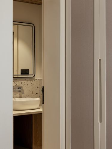 View through doorway into bathroom with oval sink, terrazzo backsplash, and framed mirror beside fabric wardrobe doors
