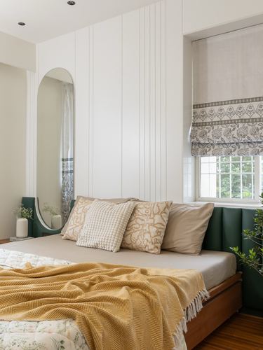 Bedroom with fluted white wall, oval mirror, green upholstered headboard, and mustard throw on bed