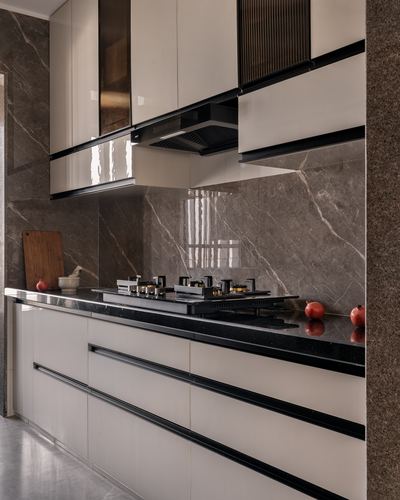 Modern kitchen with marble backsplash, black chimney hood, and glossy ivory cabinetry with pomegranates on counter